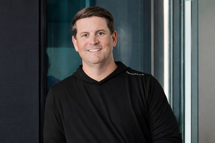Man in black hoodie standing in front of glass wall.