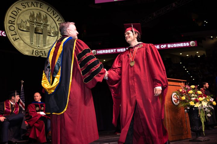 A graduate crosses the stage smiling and shakes hands with President Richard McCullough