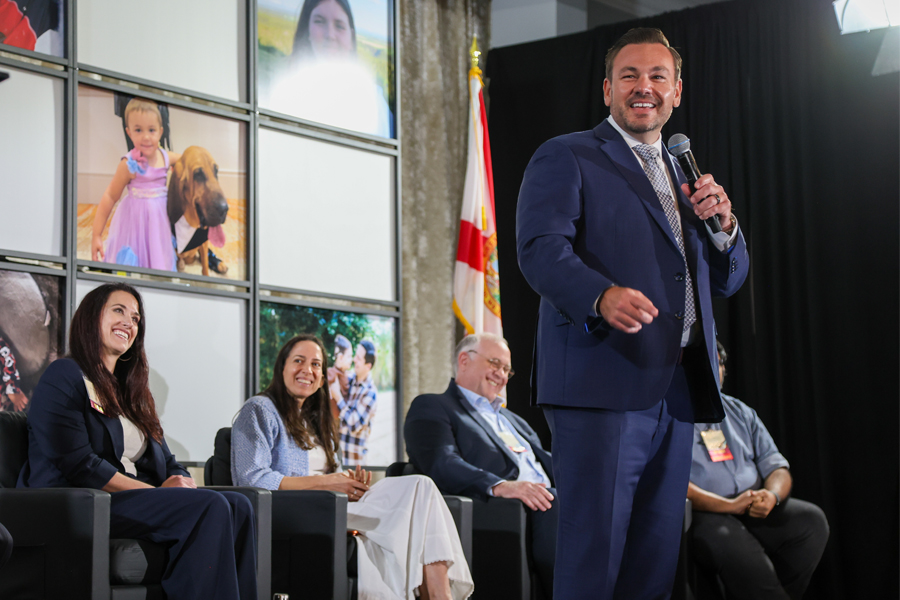 Rep. Adam Anderson holds a mic and speaks at a rare disease conference hosted by the Florida Institute for Pediatric Rare Diseases and the A.J. Anderson Foundation on Wednesday in Pinellas County. People are seated behind him.
