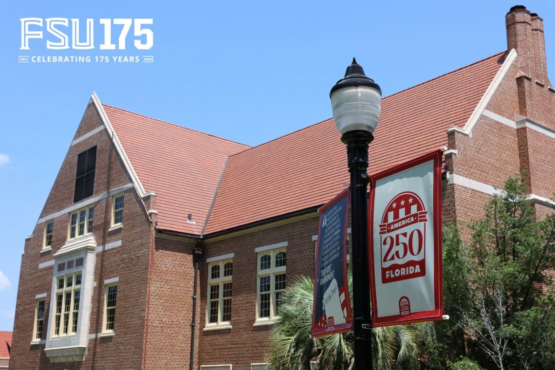 A brick campus building stands behind a lamp post displaying a red and white 