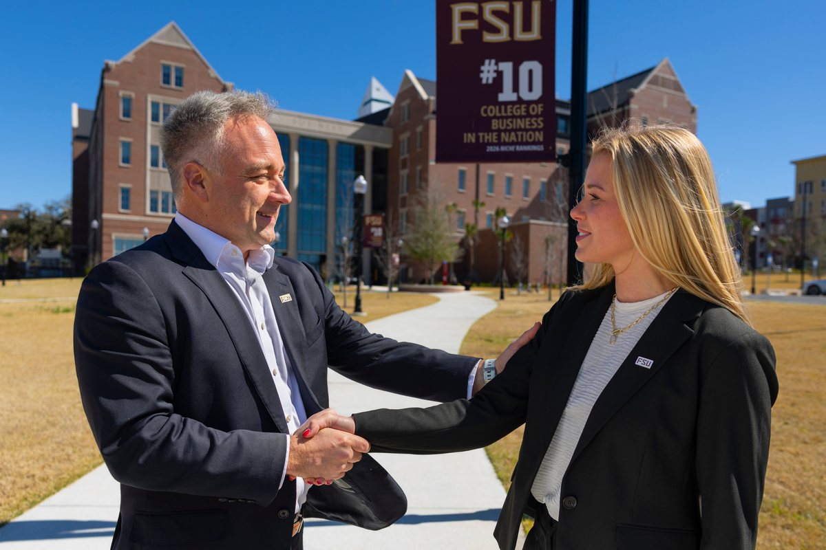 A man and woman shake hands on FSU's campus in front of a banner ranking the College of Business tenth in the nation