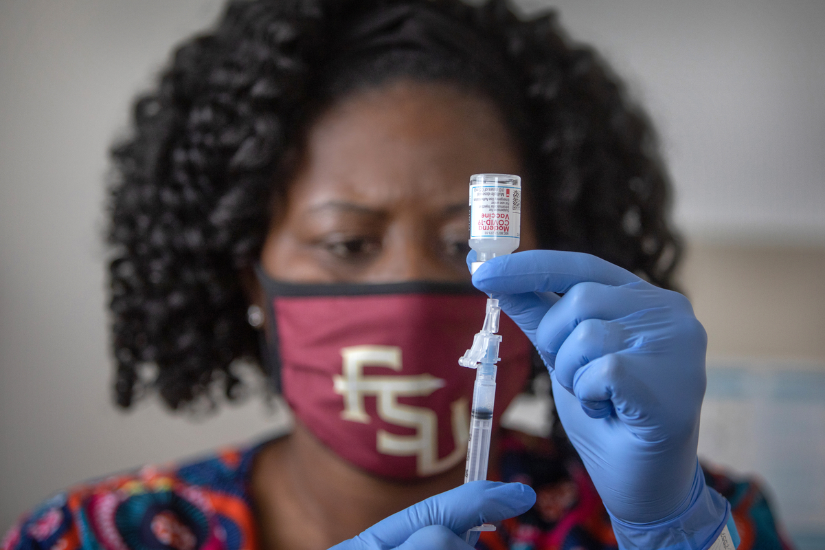 A healthcare worker wearing an FSU-branded face mask prepares a vaccine injection from a vial