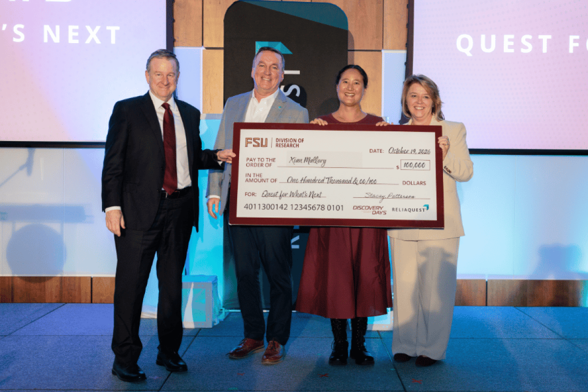 From left to right: FSU President Richard McCullough, ReliaQuest Senior Vice President of Security Operations Mike McPherson, FSU computer scientist Xian Mallory and FSU Vice President for Research Stacey Patterson pose on a stage with a big check.