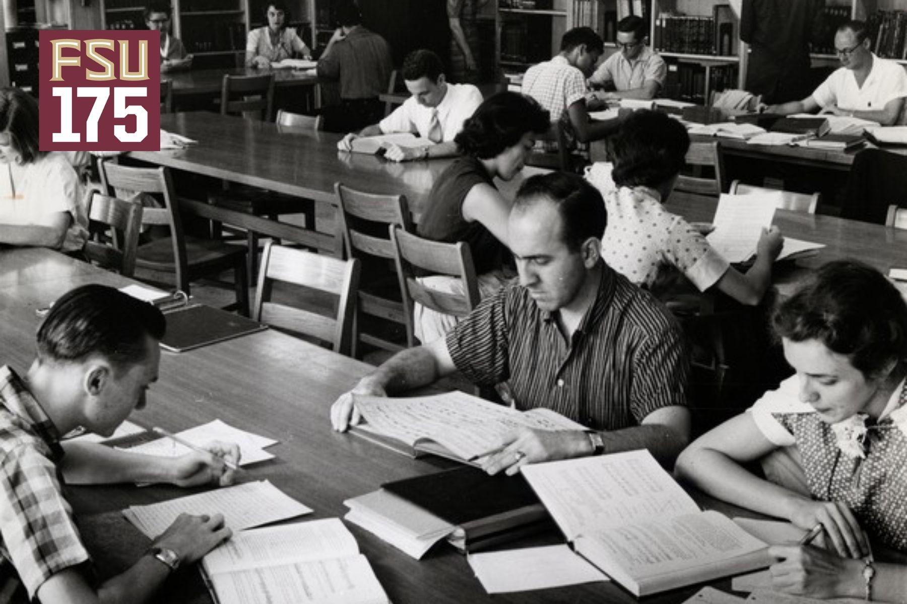 Student sit at a wood table with books and notebooks in front of them in this black and white archival photo.