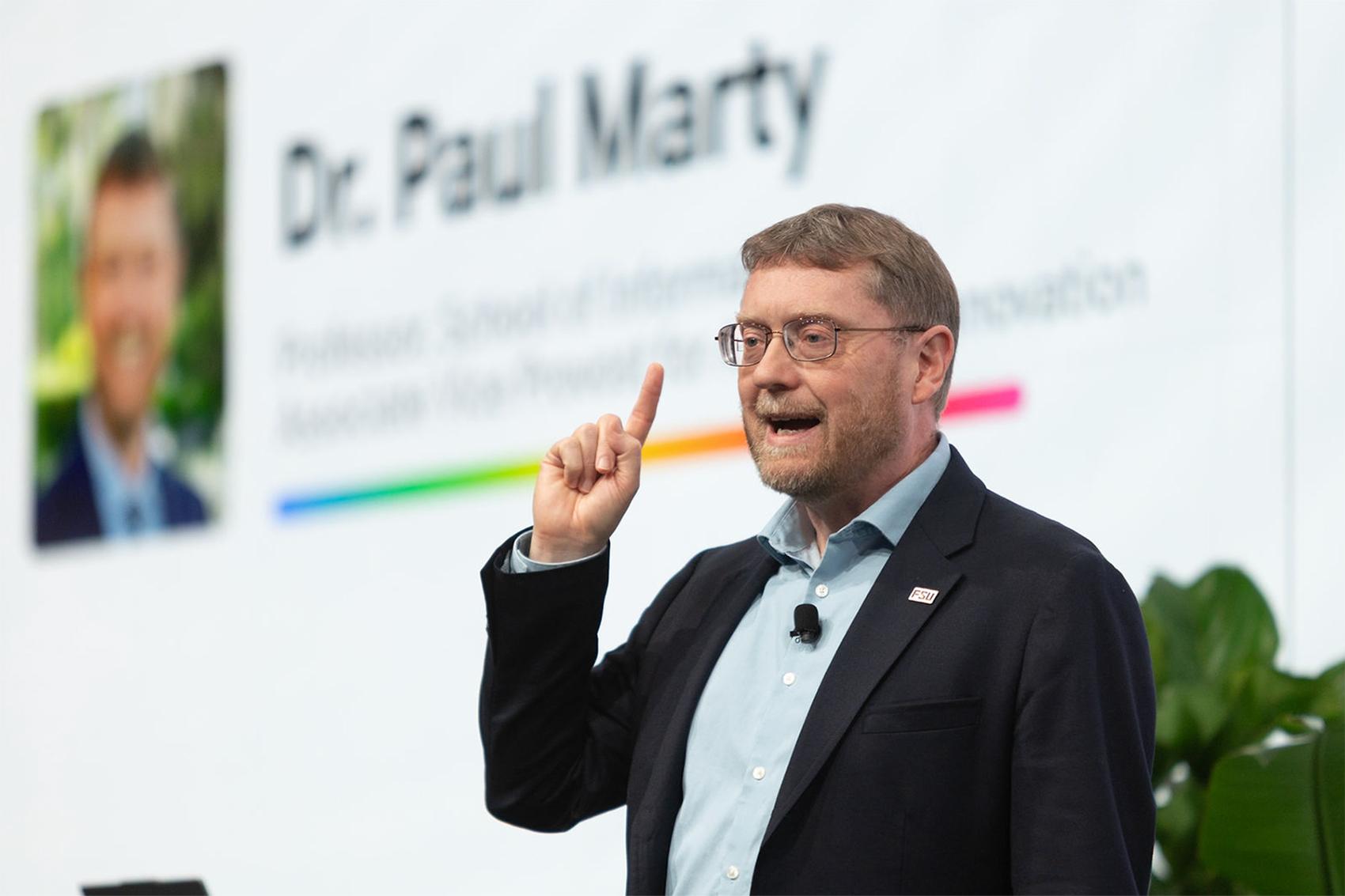 FSU's Paul Marty talks in front of a screen in front of an audience.