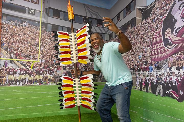 An FSU alumnus poses with the spear, the new interactive display while traveling through Tallahassee International Airport.
