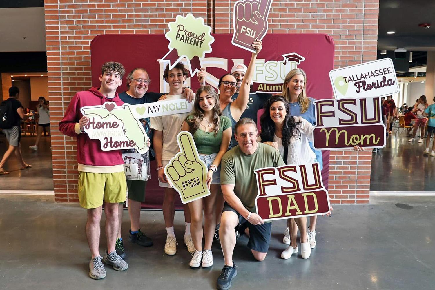 Students and parents pose with signs in front of a brick wall on campus. 
