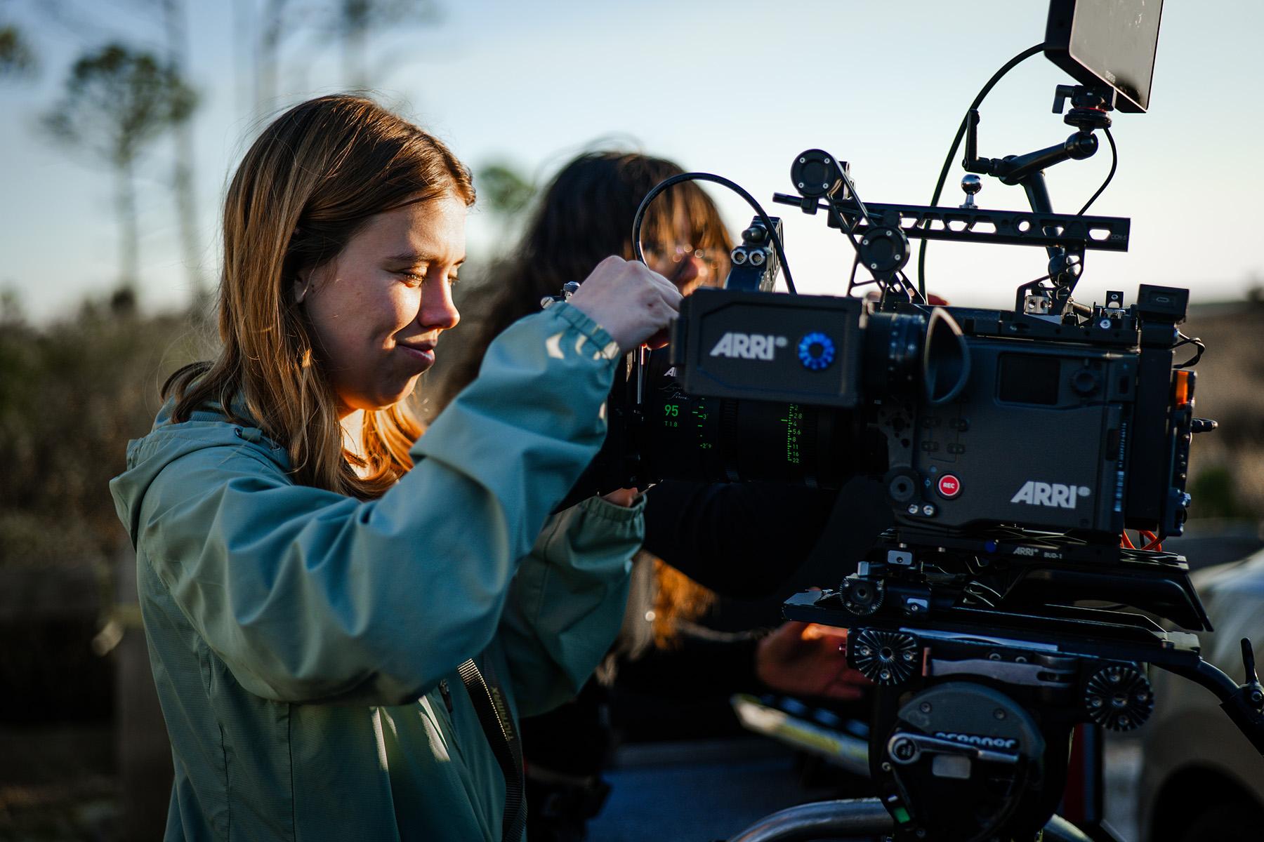 An FSU film school student in a blue jacket operates a camera in an outdoor setting.